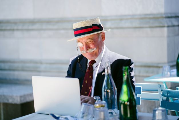 Alter Gentleman mit Strohut und Monokel vor dem nigelnagelneuen Laptop sitzend.